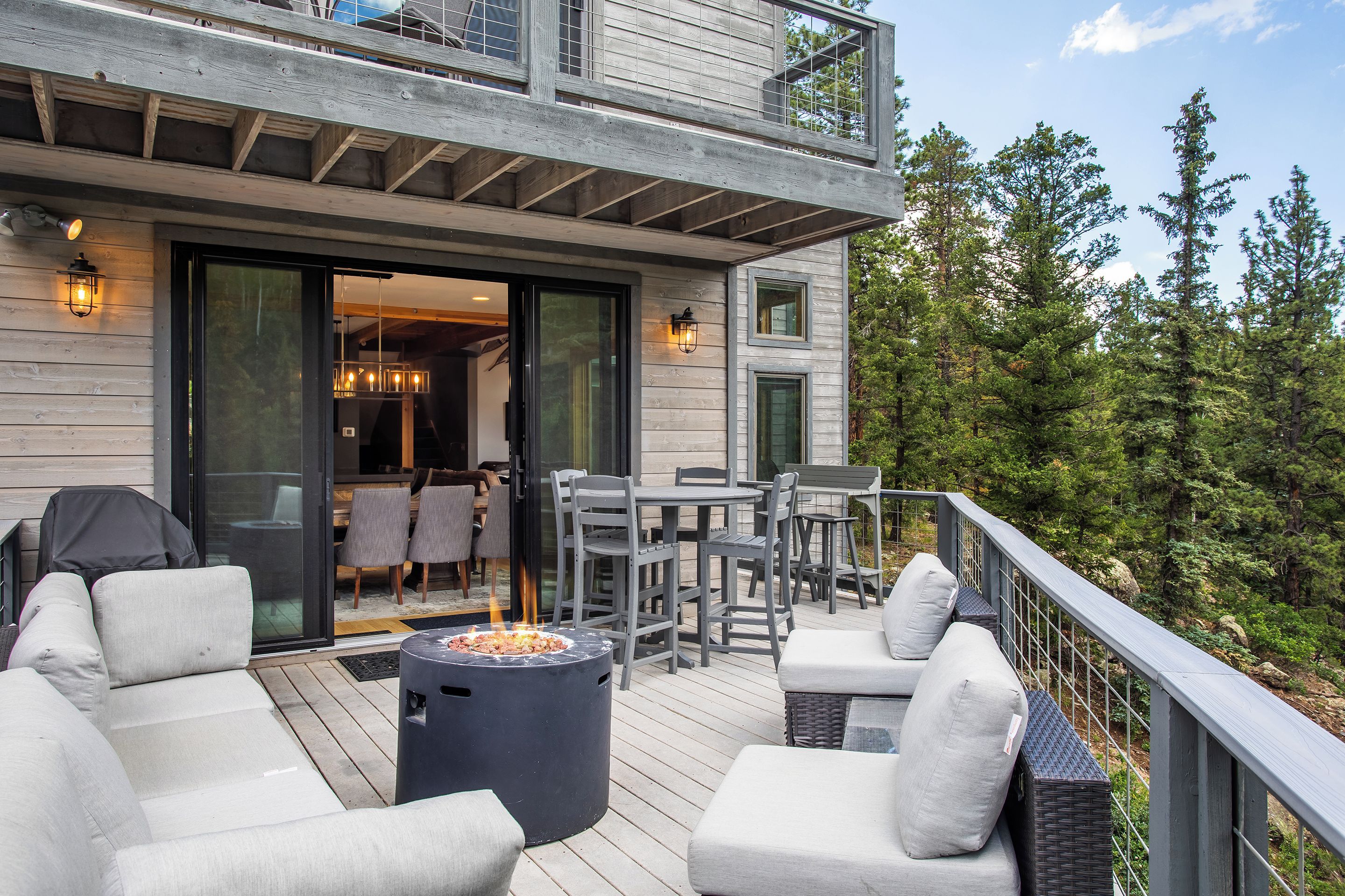 A deck with outdoor furniture, a fire pit, and a view of a forested area.