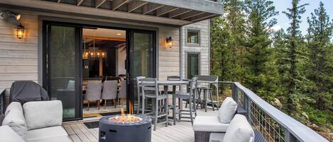 Una terraza con mobiliario exterior, una fogata y vistas a una zona boscosa.