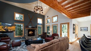 Un salón amplio con chimenea de piedra, mobiliario de cuero y grandes ventanales con vistas al exterior.