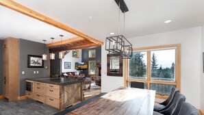 Una cocina moderna con una isla grande, vigas de madera y un amplio ventanal con vistas a árboles.