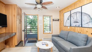 A room with a ceiling fan, a gray sofa, a white coffee table, wooden cabinets, and a large abstract painting on the wall.