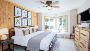A bedroom with a bed, a ceiling fan, a TV, a dresser, and framed botanical prints on the wall.