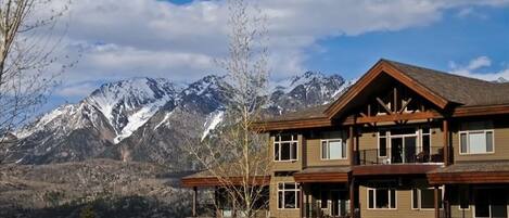 A multi-story building with balconies, set against a backdrop of snow-capped mountains and clear skies.