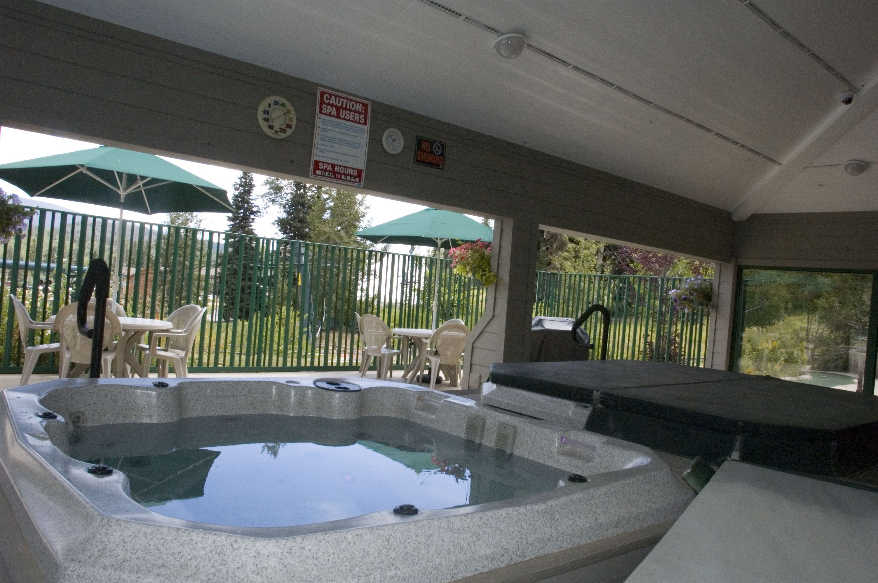 A hot tub area with a covered patio, outdoor seating, and a clock.