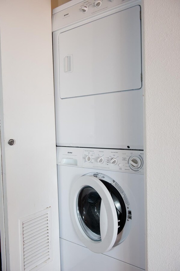 A front-loading washing machine with a control panel and a dryer stacked above it.