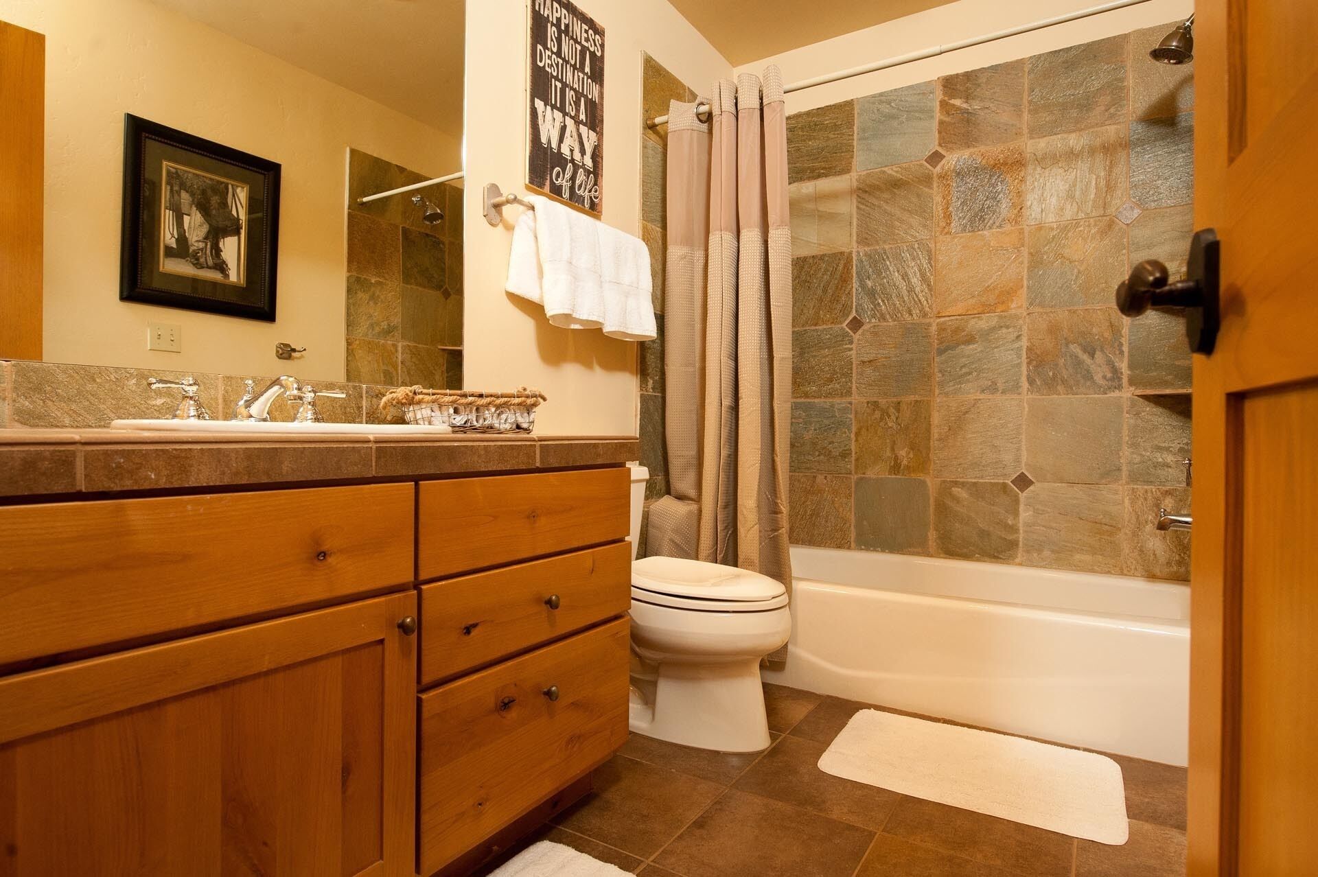 Een badkamer met een stenen douche, een wit toilet, houten kastjes en een lijst met een foto aan de muur.