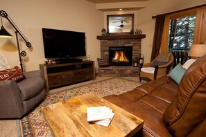 A cozy living room with a stone fireplace, a flat-screen TV, a wooden coffee table, and a leather sofa. - Black Bear Townhome - Great Views - Ping Pong - Professionally Decorated (Durango)