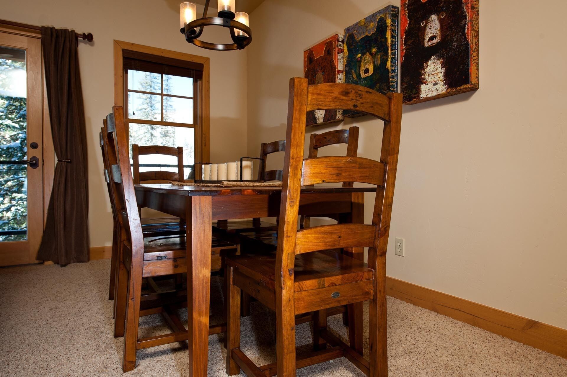 Un comedor con una mesa y sillas de madera, una araña y obras de arte en la pared.