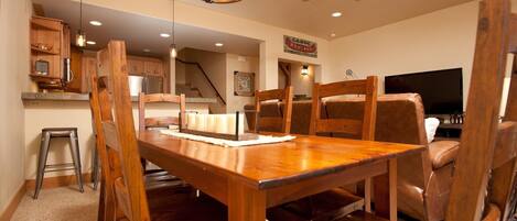 A dining area with a wooden table and chairs, a ceiling fan, and a kitchen in the background.