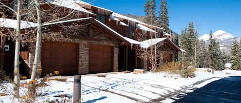 Una cabaña rústica con fachada de piedra, puertas de garaje de madera y techo cubierto de nieve.