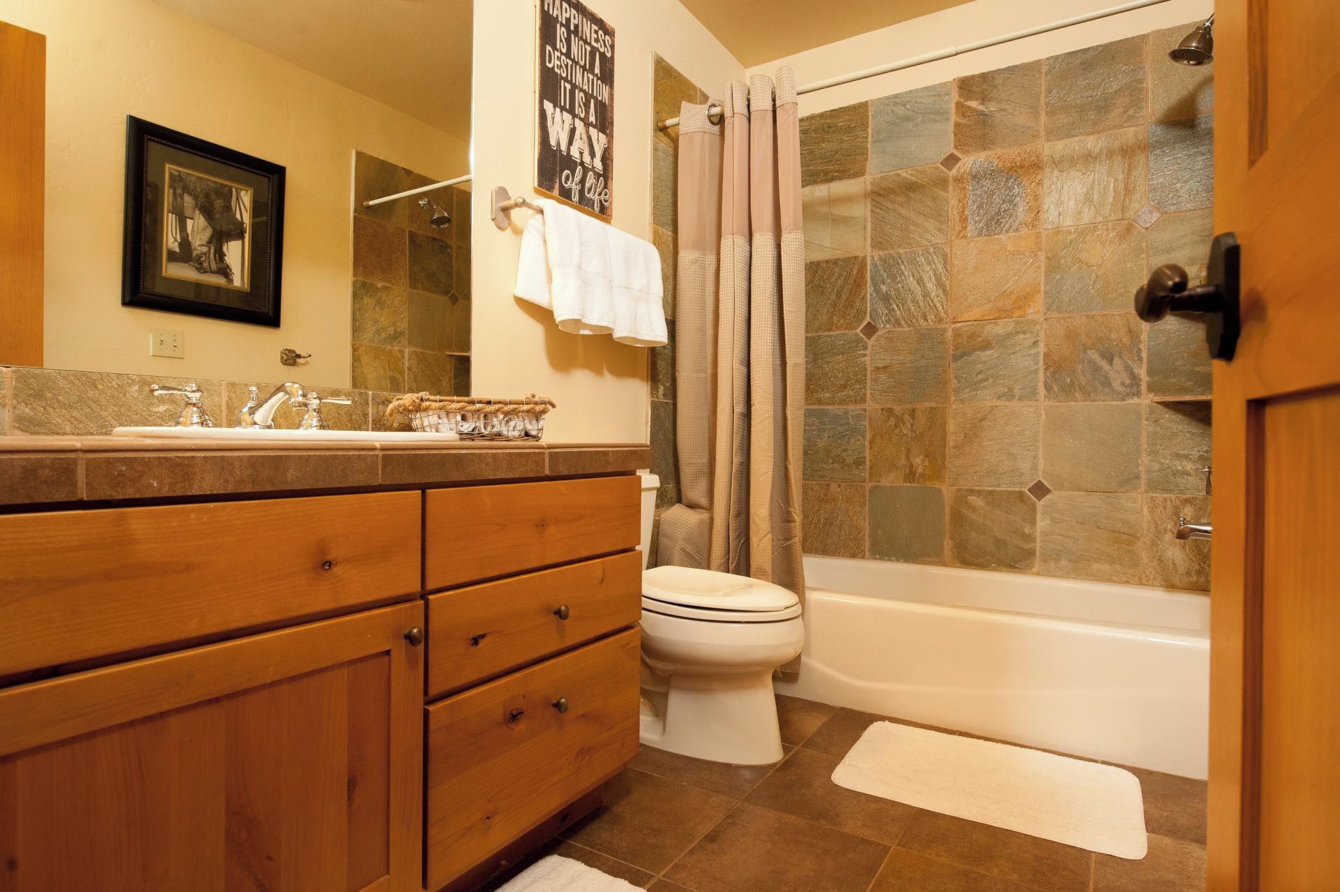 A bathroom with a stone shower, a white toilet, wooden cabinets, and a framed picture on the wall.