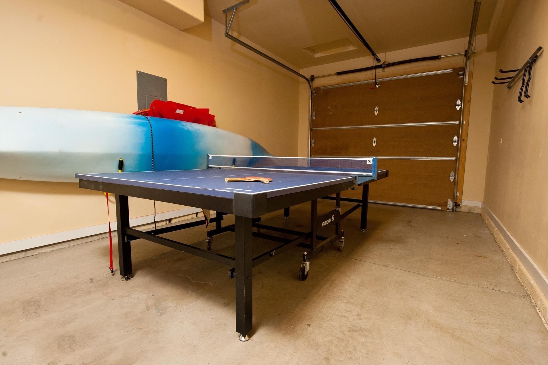 A ping pong table in a room with a concrete floor, a door, and a wall-mounted rack.