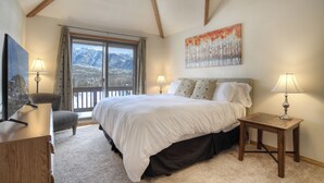 Ein Schlafzimmer mit einem großen Bett, zwei Nachttischlampen, einem Holznachttisch, einem Sessel und einem Gemälde.