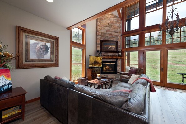 A spacious living room with a stone fireplace, large windows, and a cozy seating area.