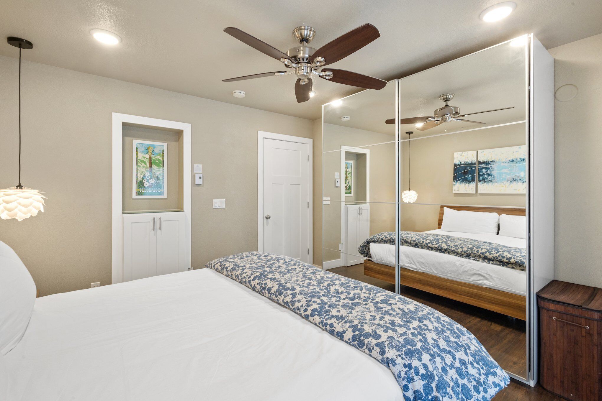 A bedroom with a large bed, a ceiling fan, a wardrobe, and a mirror.