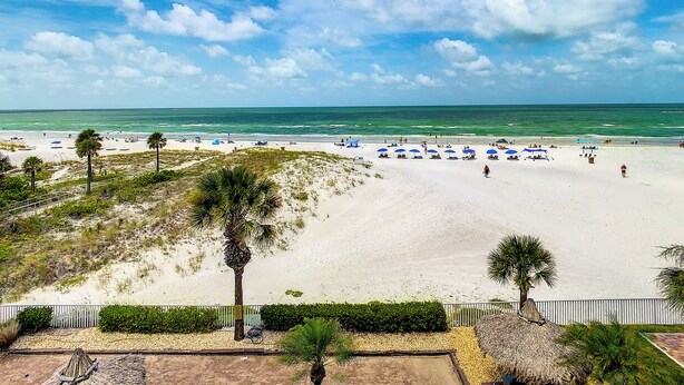 A beach with white sand, palm trees, and a clear blue sky.