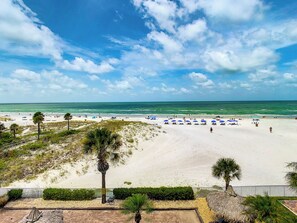 A beach with white sand, palm trees, and a clear blue sky.