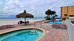 A pool area with lounge chairs and umbrellas, a pool, and a view of the ocean.