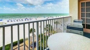 A balcony with a view of the beach, a table, and a chair.