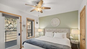 A bedroom with a bed, a ceiling fan, a nightstand with a lamp, a door with a view, and a wall with a decorative plate. - River view condo w/ hot tub + pool (Telluride)