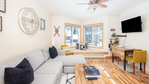 A modern living room with a sectional sofa, a wooden coffee table, a TV mounted on the wall, and a ceiling fan. - River view condo w/ hot tub + pool (Telluride)
