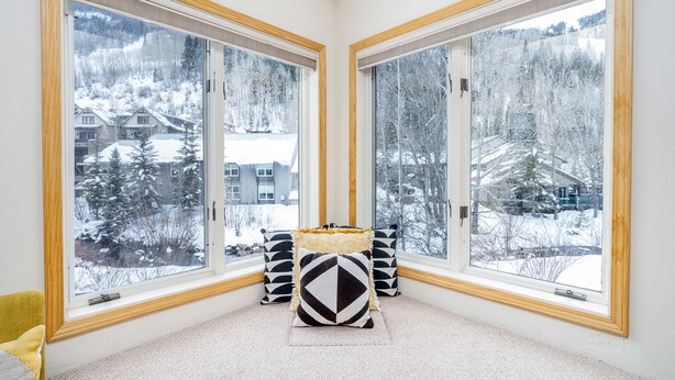 A corner room with large windows, a small table with cushions, and a view of a snowy landscape. - River view condo w/ hot tub + pool (Telluride)
