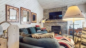 Una sala de estar acogedora con chimenea de piedra, un televisor montado encima y una lámpara de pie grande.