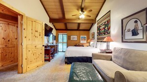 Une pièce confortable avec un lit, une porte en bois, un téléviseur et un ventilateur de plafond.