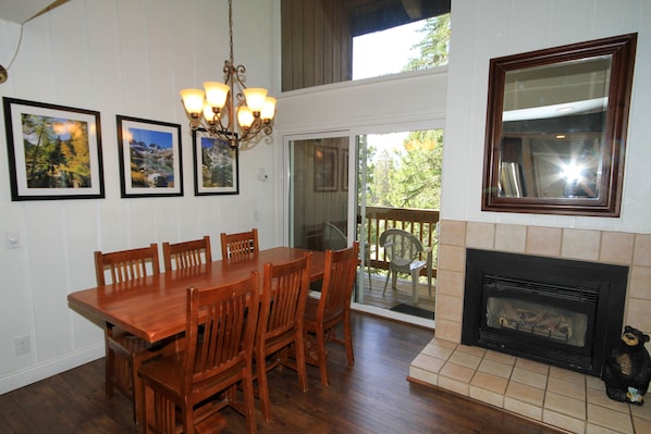 A dining area with a wooden table and chairs, a chandelier, framed pictures on the wall, and a fireplace.