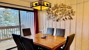 Un comedor con una mesa de madera y sillas negras, un adorno en la pared y vistas a través de un amplio ventanal.