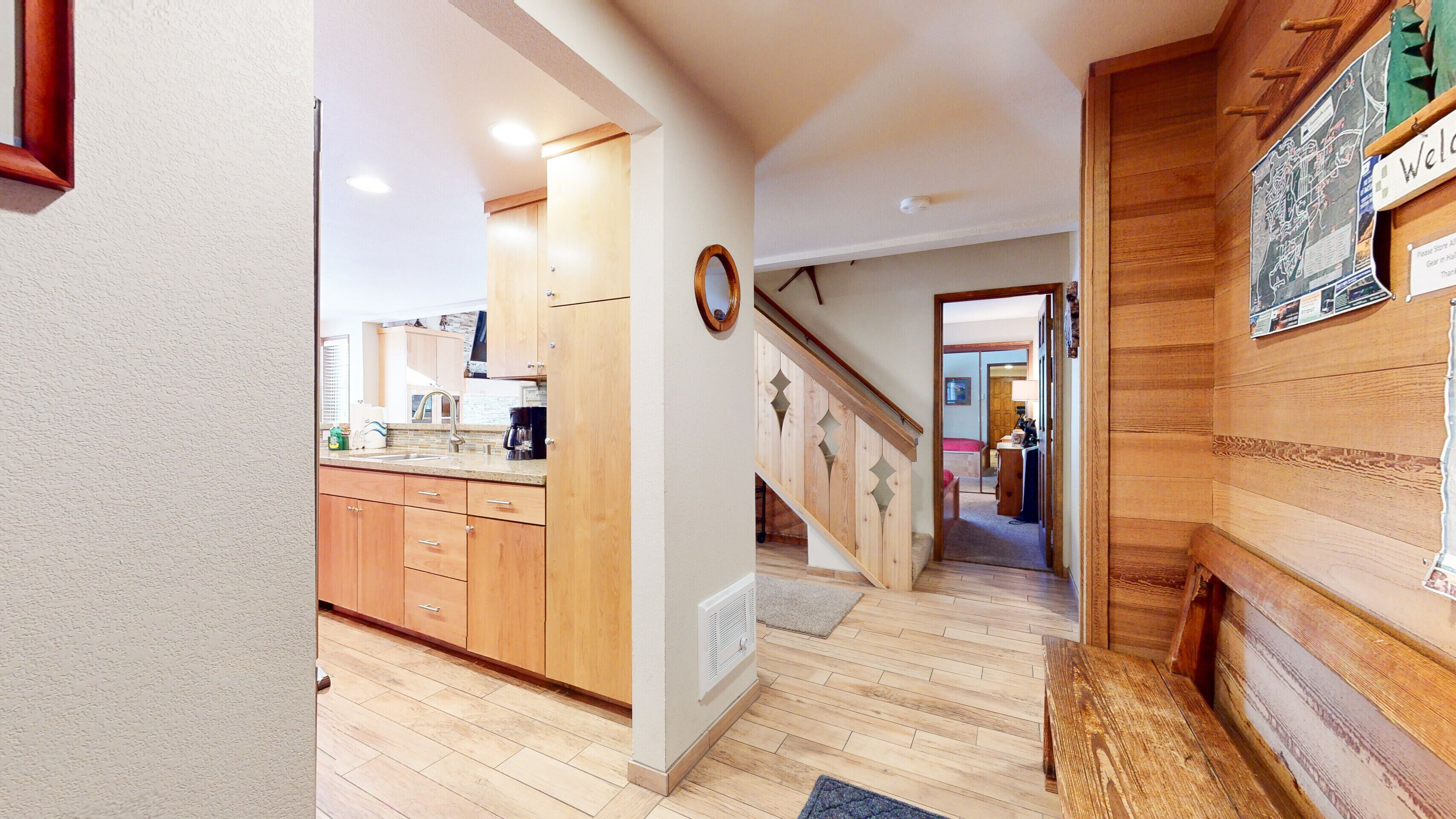 Un couloir doté d’un plancher en bois, un coin cuisine avec des meubles en bois, et un escalier menant à une autre pièce.