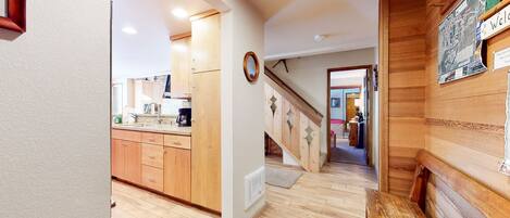 Un couloir doté d’un plancher en bois, un coin cuisine avec des meubles en bois, et un escalier menant à une autre pièce.