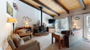 A cozy living room with a fireplace, comfortable seating, a television, and a view of the outdoors. - Cozy Mountain Home, Shuttle Route, Walk to Bowling Alley & Washer/Dryer (Mammoth Lakes)