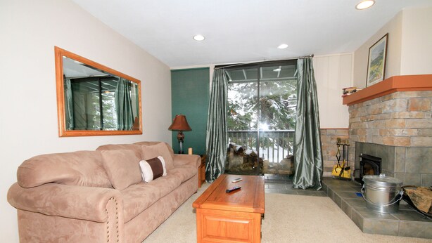 A living room with a beige sofa, a wooden coffee table, a fireplace, and a large window with curtains.