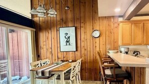 A wooden interior with a dining table and chairs, a kitchen area with wooden cabinets, a clock, and a framed picture on the wall. - Mammoth Ski & Racquet Club #120 - Pet Friendly (Mammoth Lakes)