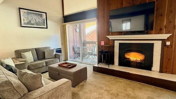 A living room with a fireplace, a sofa, a coffee table, and a television mounted above the fireplace. - Mammoth Ski & Racquet Club #120 - Pet Friendly (Mammoth Lakes)