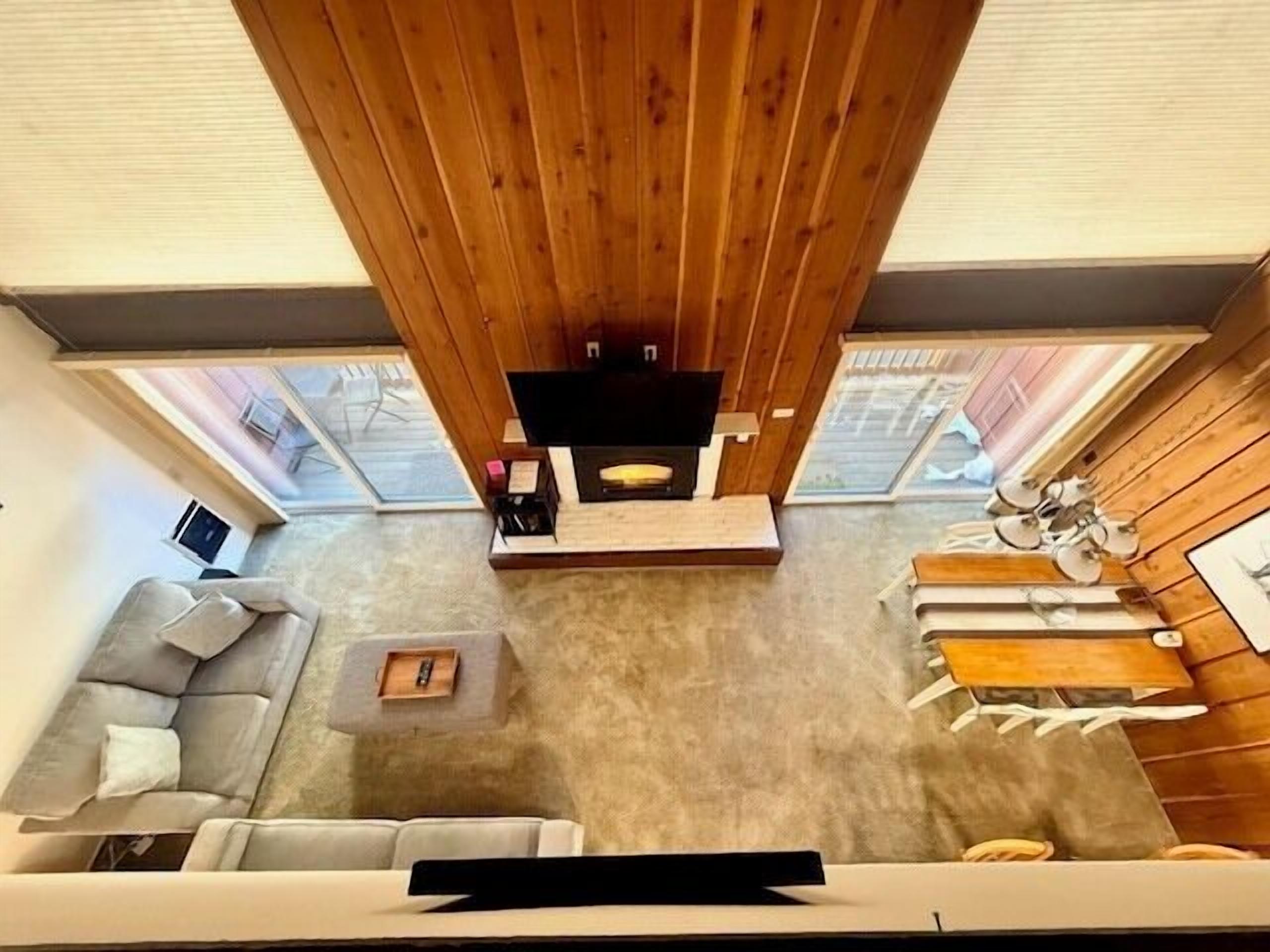 A modern living room with a wooden ceiling, a flat-screen TV, a grey sofa, a coffee table, and a dining area with a table and chairs.