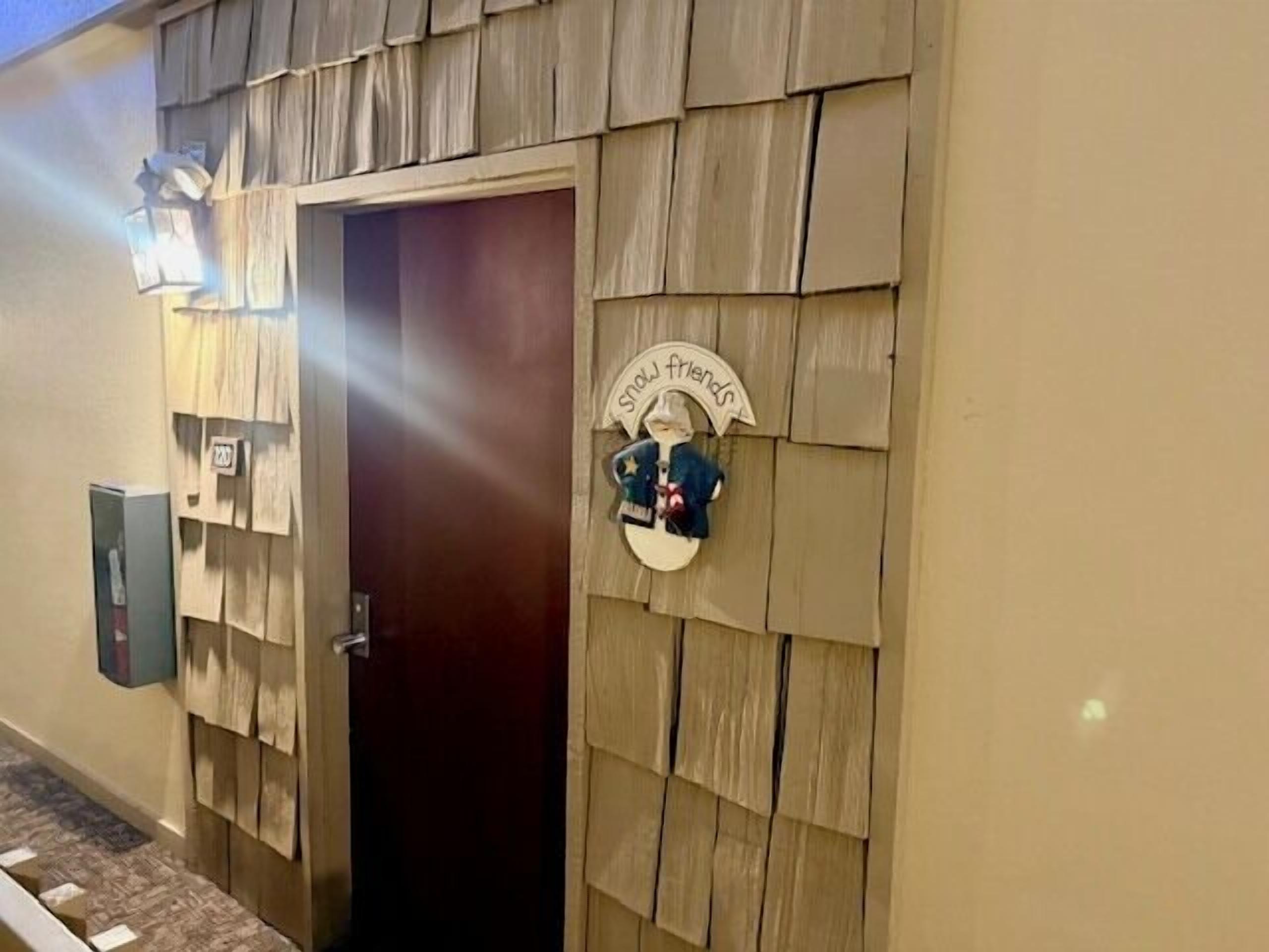 A hotel entrance with a wooden shingled facade, a dark wooden door, and a sign that reads "Stay friends."