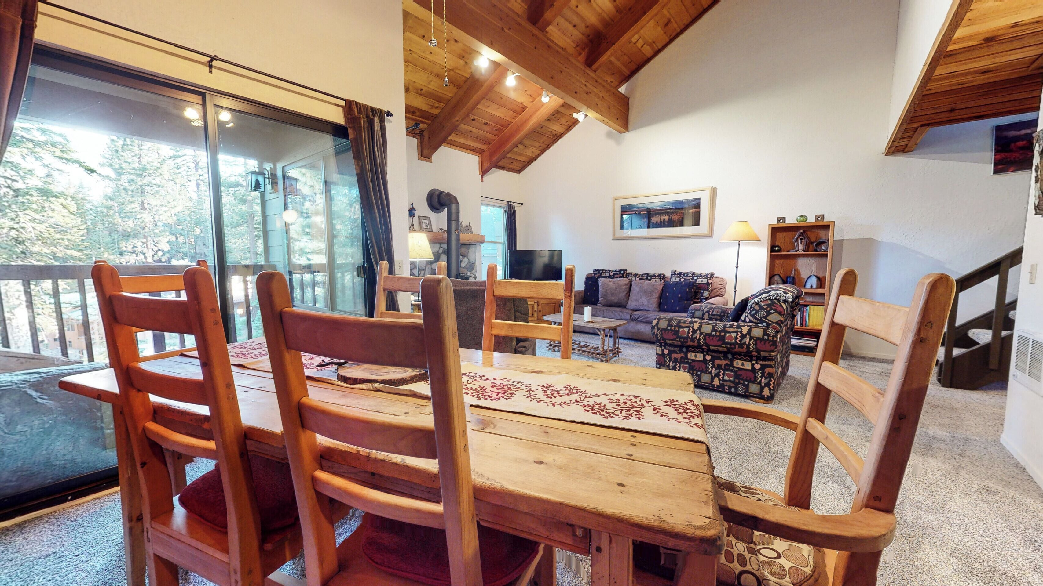 Ein Holzespeisesaal mit Stühlen, eine Couch und ein Fernseher in einem Wohnzimmer mit Kamin aus Stein und einem großen Fenster.
