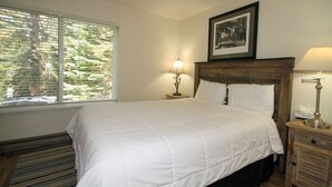 Una cama bien hecha con ropa de cama blanca, cabecera de madera y mesita de noche con lámpara.
