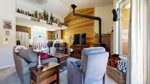 A cozy living room with a fireplace, a television, and a kitchen in the background. - Renovated Forest Retreat, Private Hot Tub, Washer/Dryer & Peaceful Setting (Mammoth Lakes)