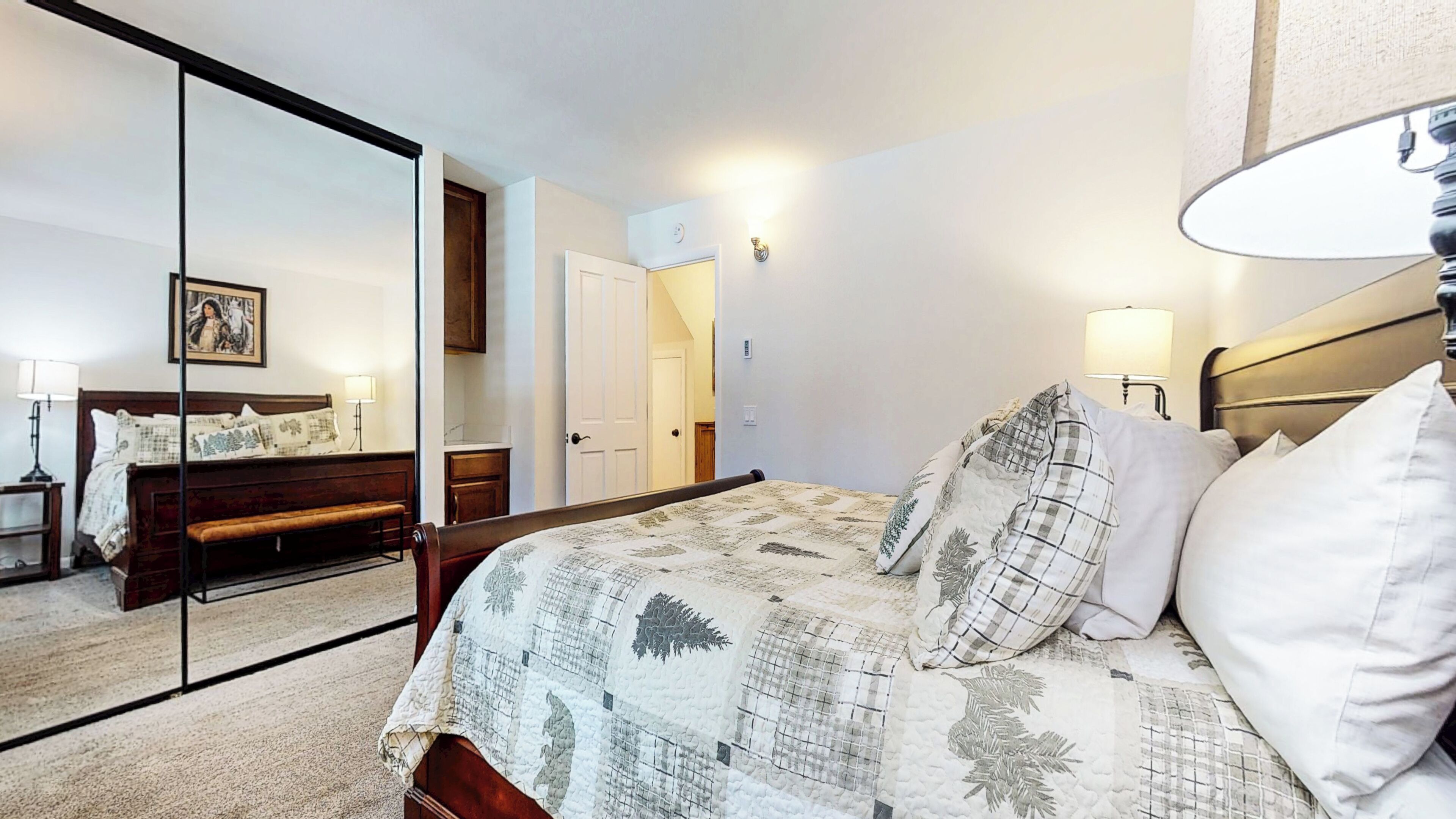 Une chambre à coucher avec un lit, des lampes de chevet, un miroir, une porte et un tableau accroché au mur.