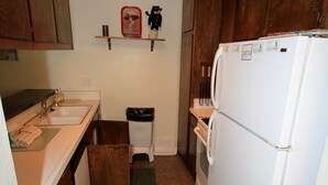 Eine kleine Küche mit Holzausstattung, einem weißen Kühlschrank und einer kleinen Mülltonne.