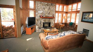 A cozy living room with a stone fireplace, wooden furniture, and large windows. - Mountainback #63, Loft, Den (Mammoth Lakes)