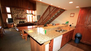 A kitchen with granite countertops, wooden cabinets, a dishwasher, and a stone fireplace. - Mountainback #63, Loft, Den (Mammoth Lakes)
