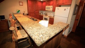 A kitchen with wooden cabinets, granite countertops, a microwave, a stove, and a refrigerator. - Mountainback #63, Loft, Den (Mammoth Lakes)