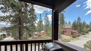 Ein Holzbalkon mit Grill, mit Blick auf eine Wohngegend mit Häusern und Bäumen.