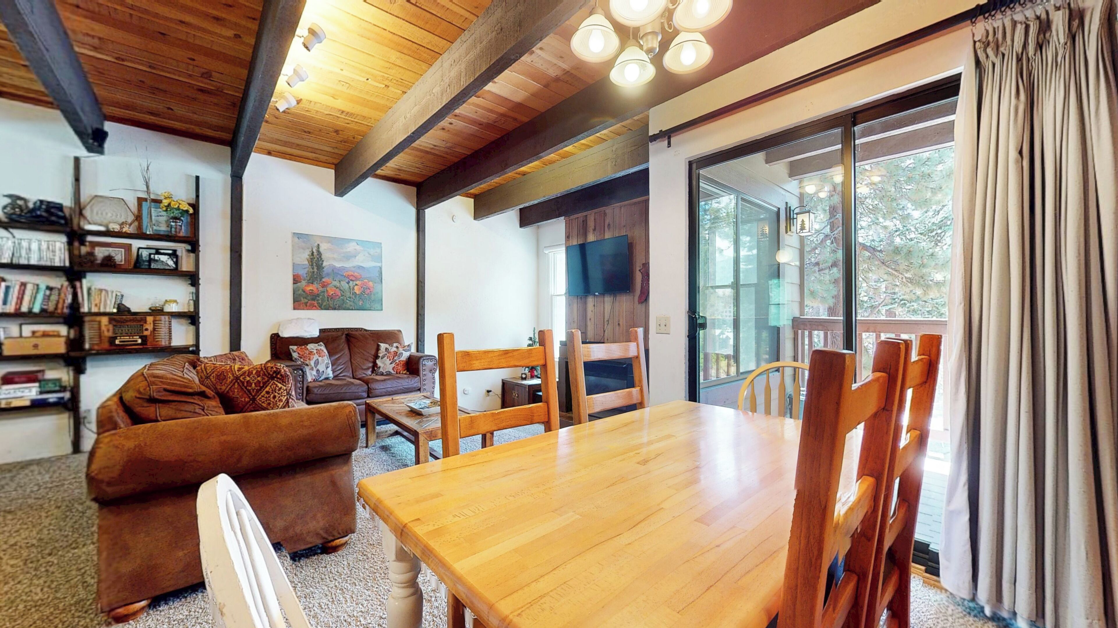 A cozy living room with a wooden table, chairs, a sofa, and a bookshelf.