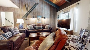 A cozy living room with leather sofas, a coffee table, a TV, and a wooden wall with a poster. - Mountain Rustic, Pool & Tennis, Near Dining, Rec Center, Bowling & Trails (Mammoth Lakes)