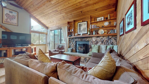 Una sala de estar acogedora con chimenea de piedra, techo de madera y televisor sobre un mueble de madera.